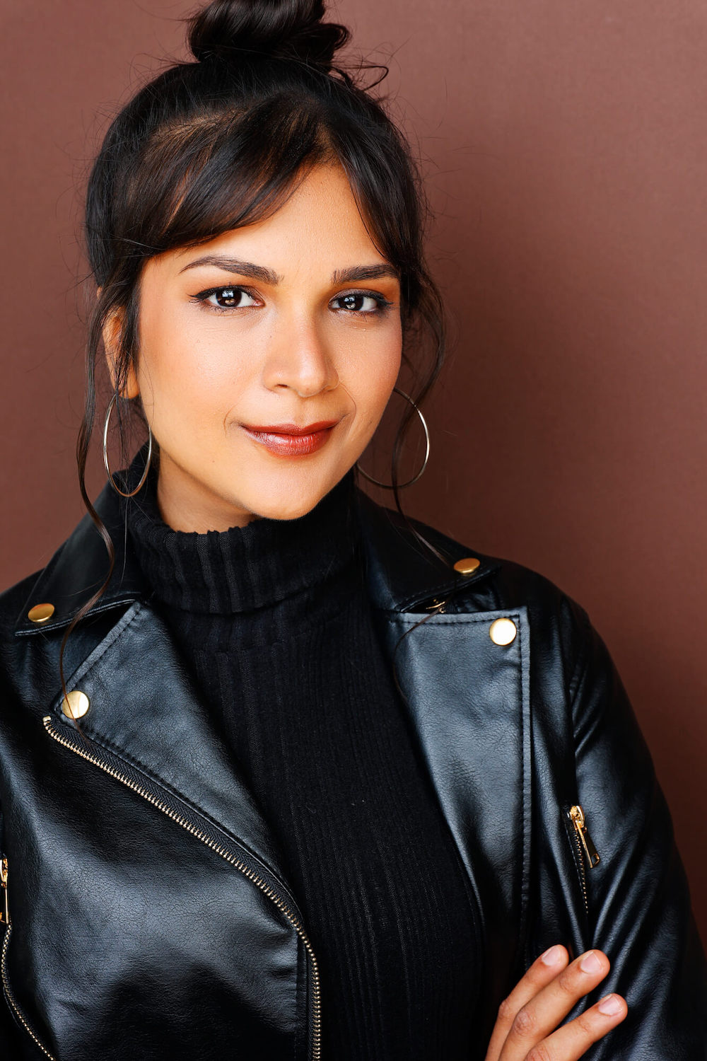 Half-body shot of Shivani Desai in a black leather jacket and turtleneck, against a dark red wall.