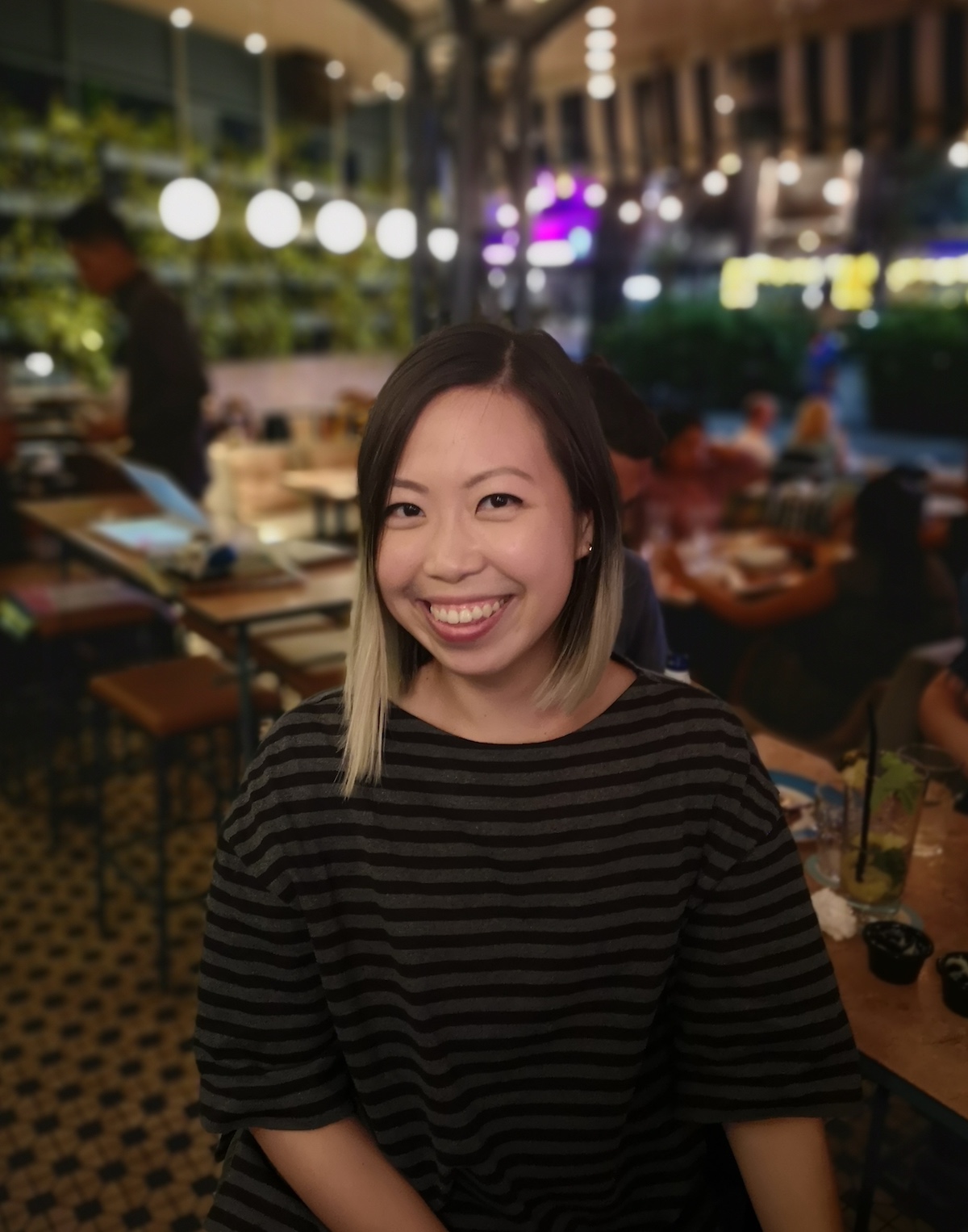 Half-body shot of Corrie Tan at a restaurant, wearing an elbow-length shirt, smiling.