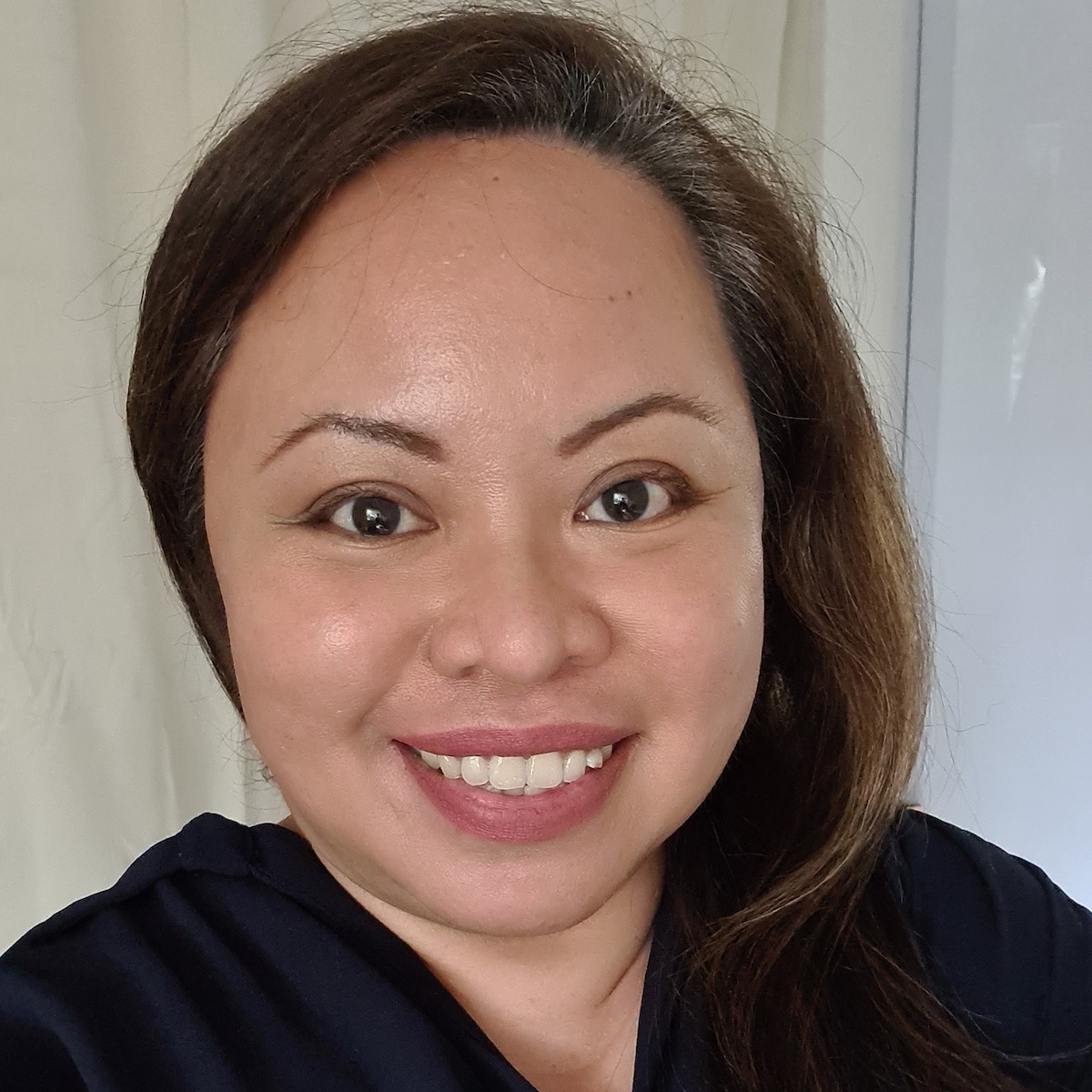 Headshot of Elnie Mashari in front of a beige curtain, smiling into the camera.