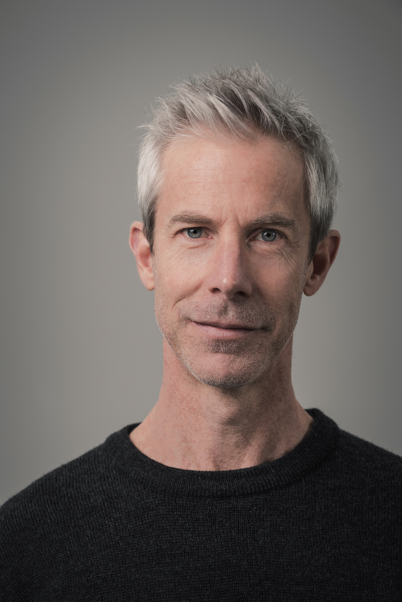 Headshot of Jonathon Young against a grey background, wearing a black shirt.