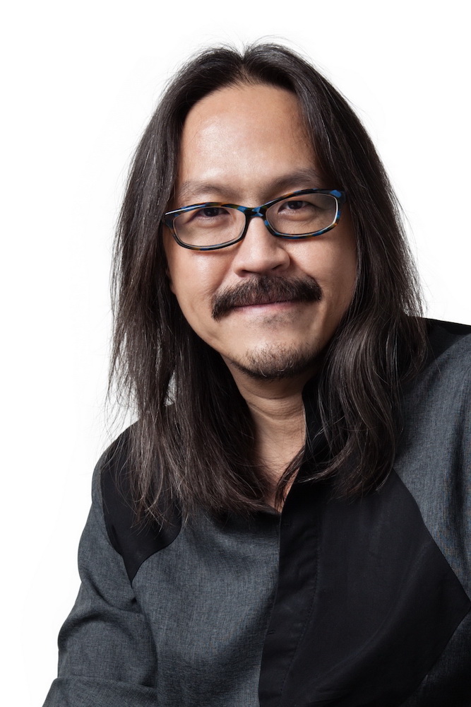 Half-body shot of Pawit Mahasarinand in glasses, with a moustache and long hair.