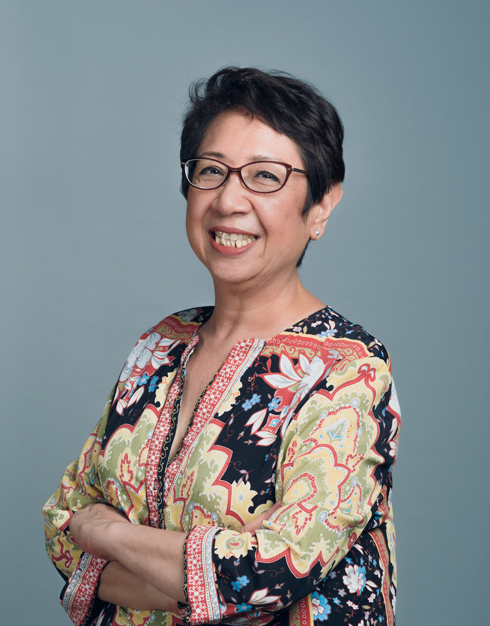 Half-body shot of Peggy Ferroa in a colourful top, arms folded, smiling.