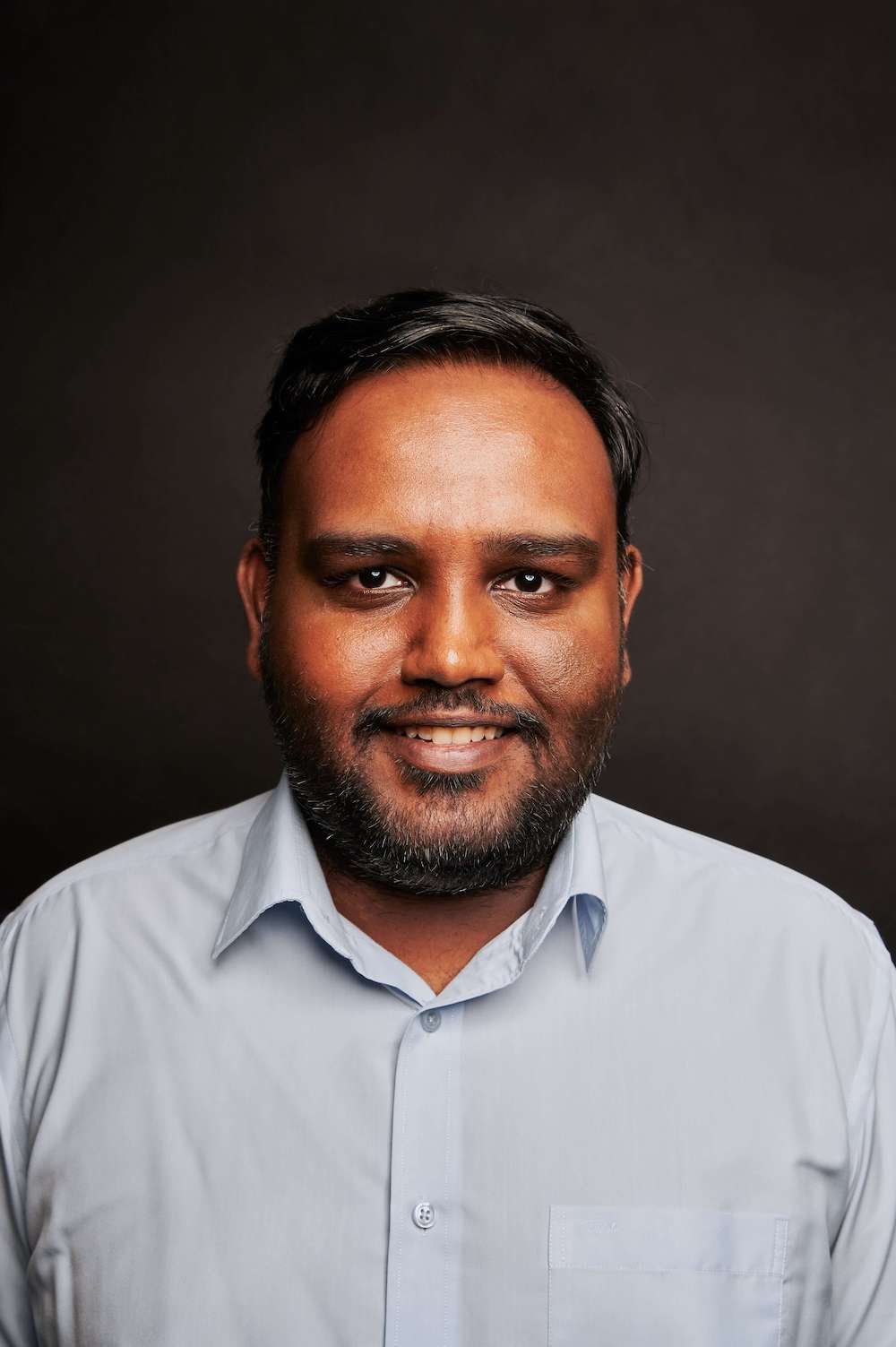 Half-body shot of Rajkumar Thiagaras in a blue collared shirt, smiling into the camera.