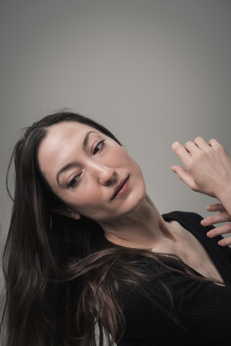 Half-body shot of Renee Sigouin, head tilted back, hands crossed above her chest, glancing downwards.