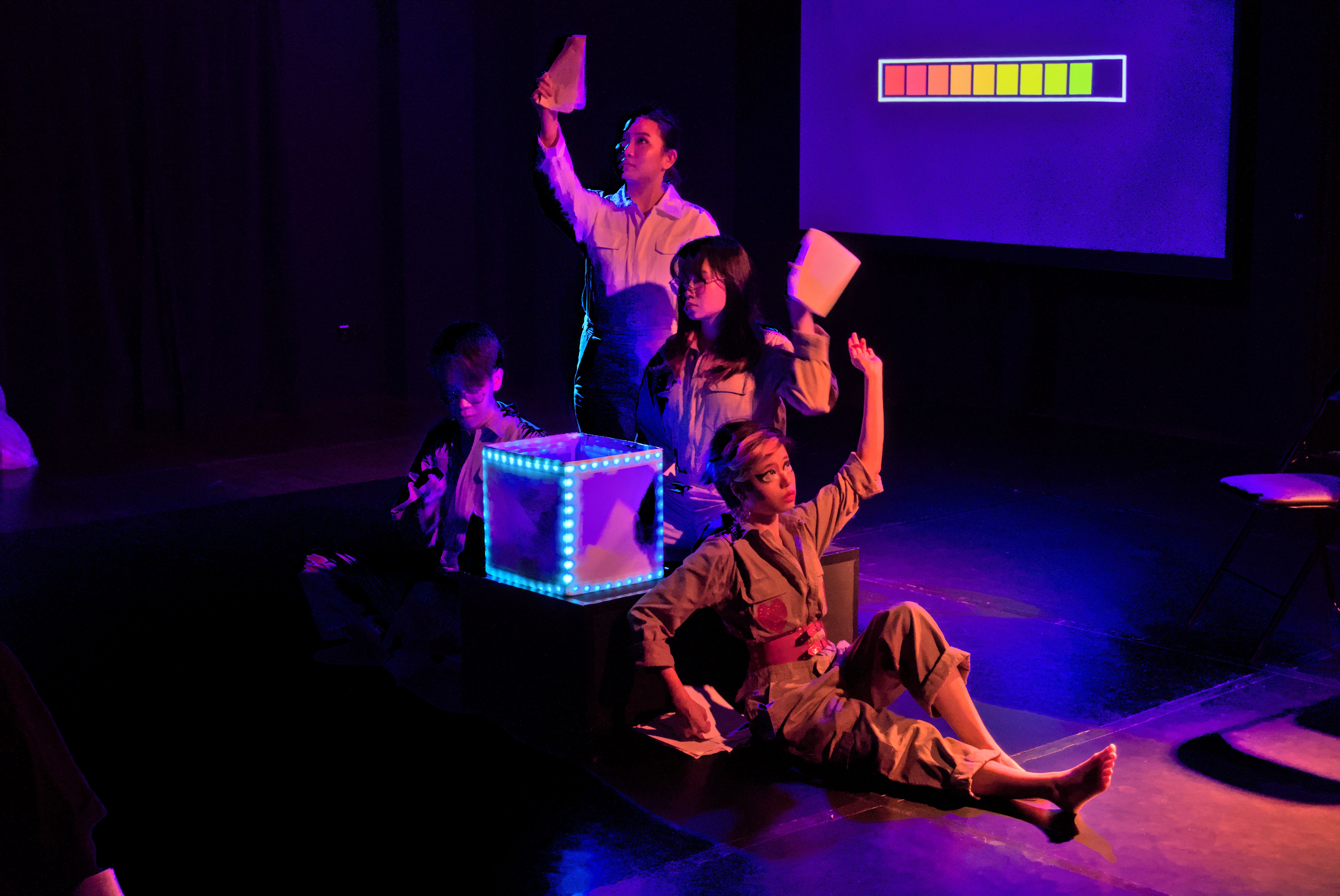 Four persons gathered around a glowing box, holding and passing papers to one another.