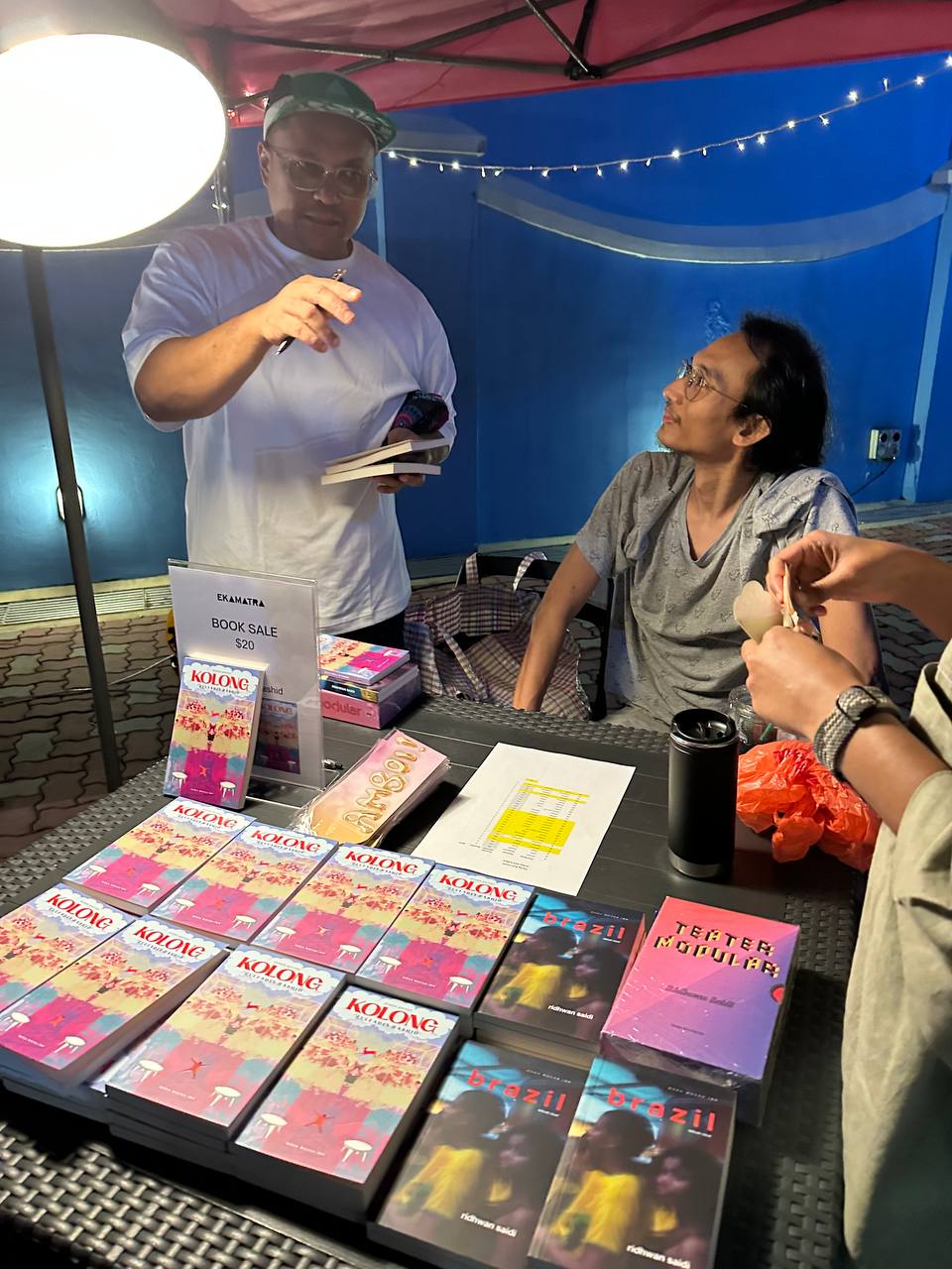 A photograph of Zulfadli Rashid and Ridhwan Saidi from Moka Mocha Ink at a table with books laid out in front of them.