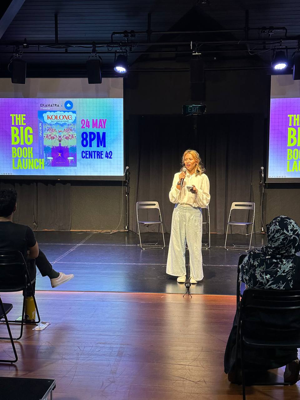 A photograph of Nabilah Said holding a microphone against a backdrop of screens with the event poster for the Big Book Launch.