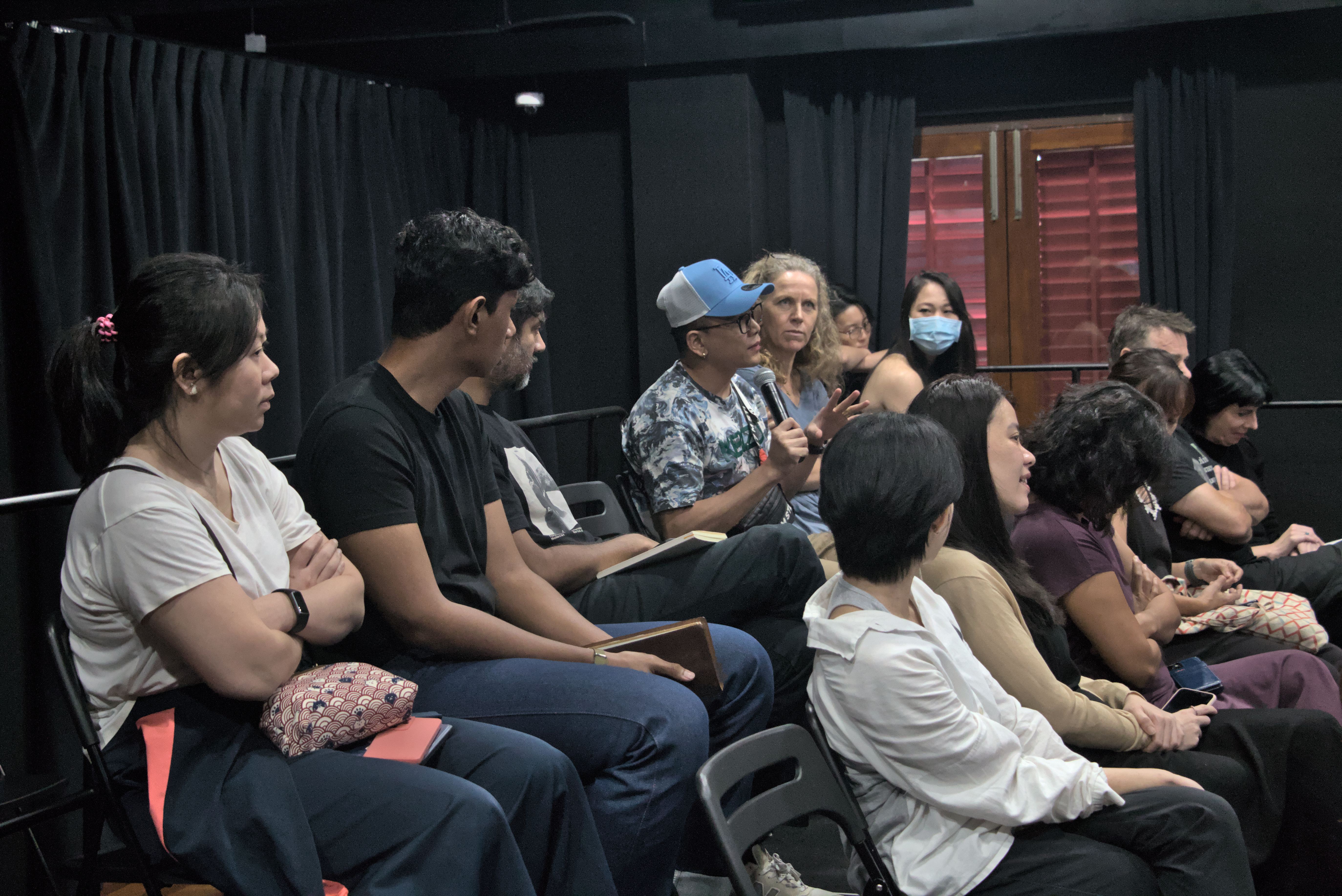 An image of audience members at the roundtable dialogue, one raising a question to the panel with mic in hand. 