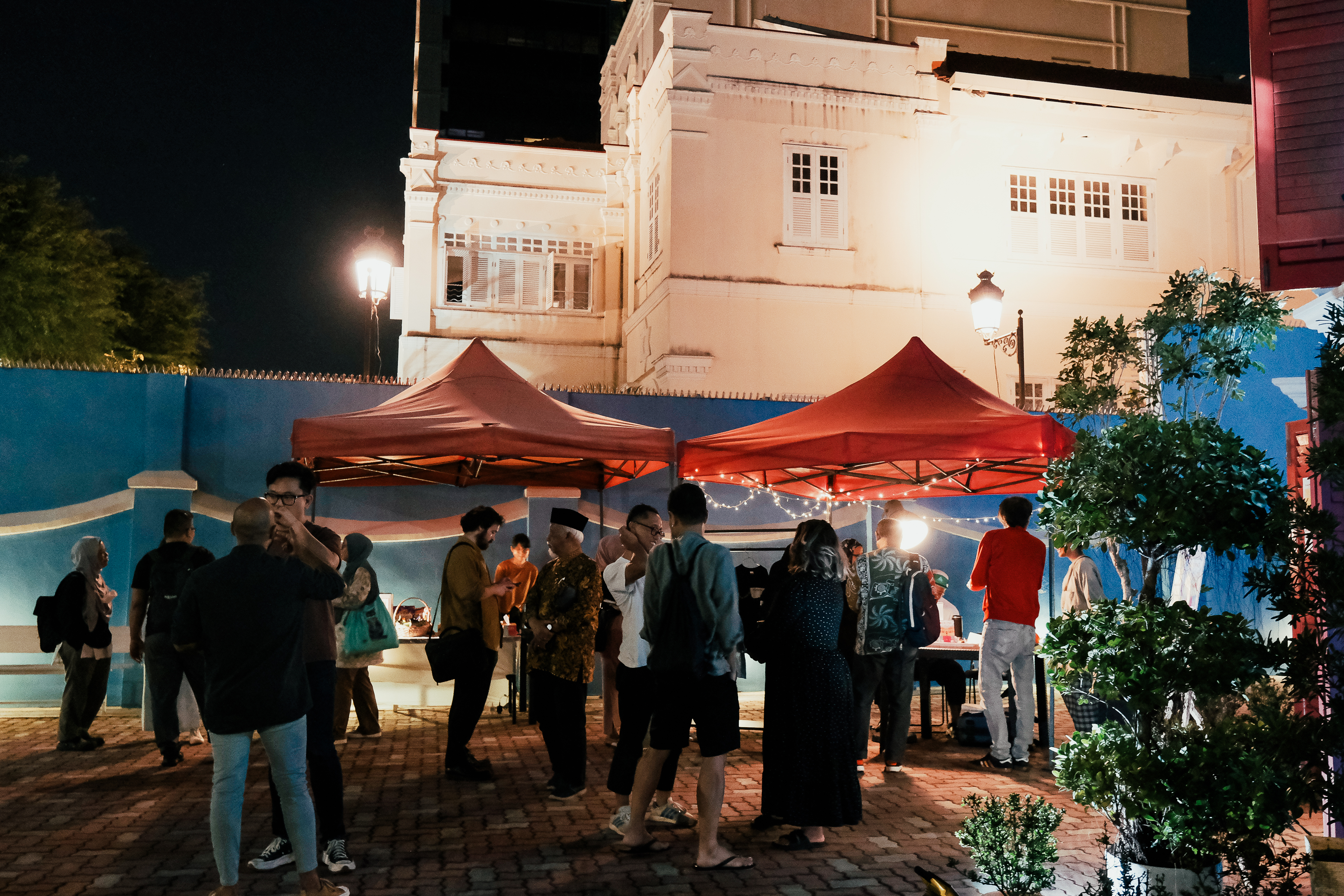 A photograph of a crowd of people in front of two red gazebos at the front courtyard of 42 Waterloo Street.