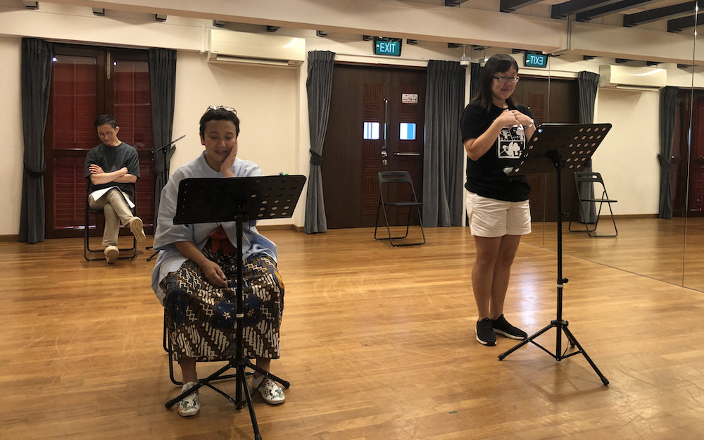 A female-presenting person seated in front of a music stand. To her right, another female-presenting person standing in front of a music stand.