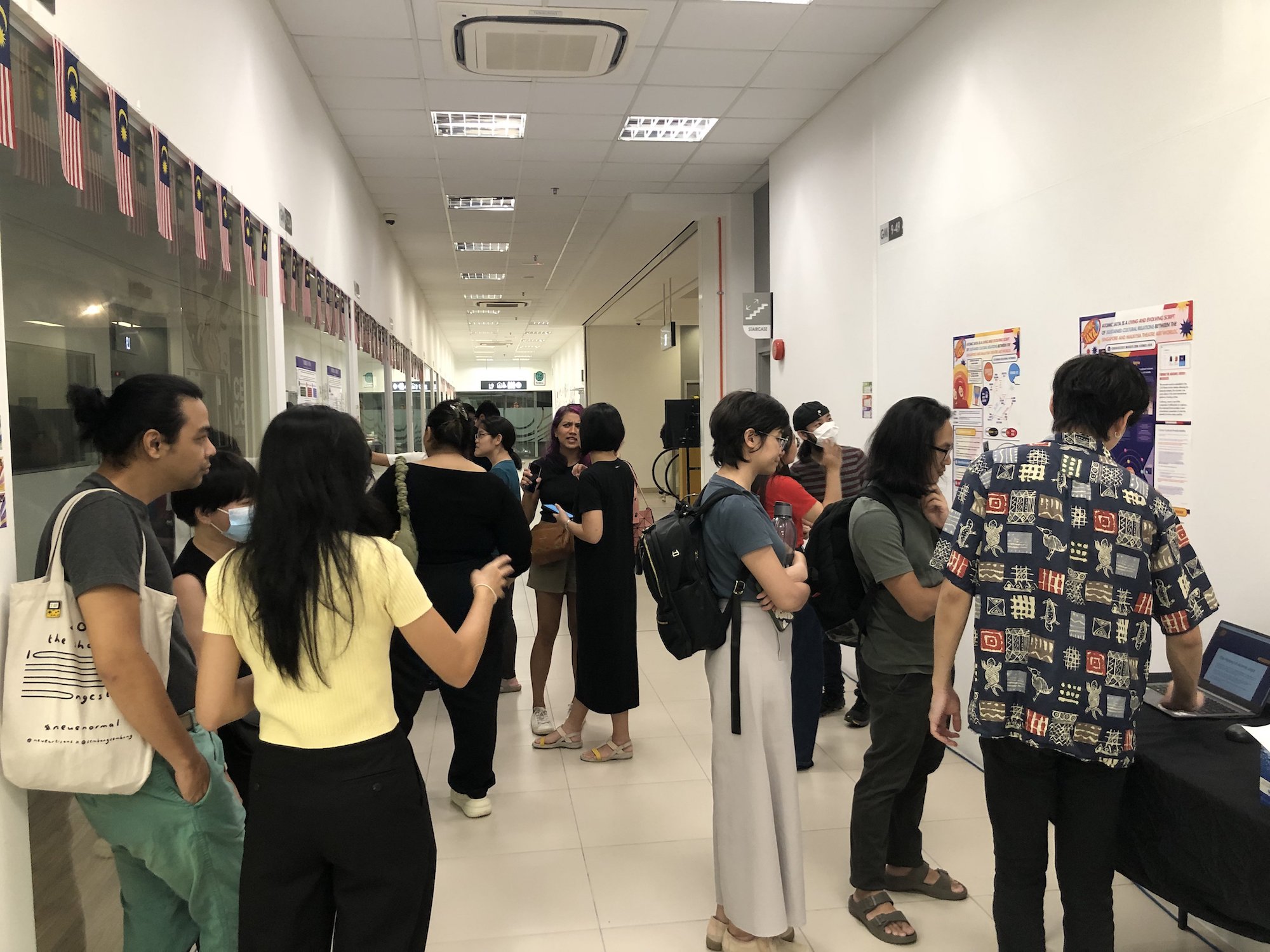 A large group of people mingling in a corridor lined with posters.