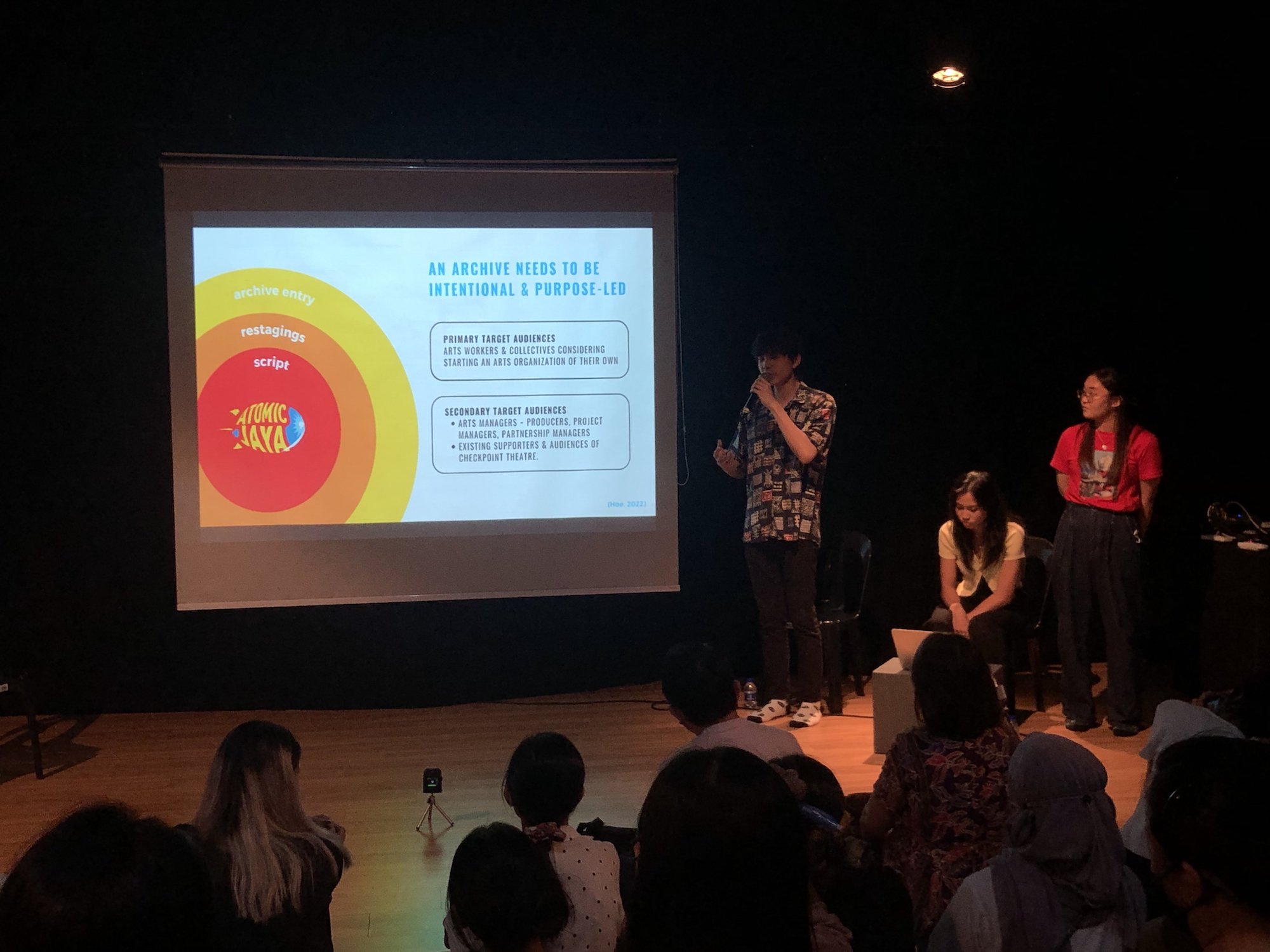 Three persons standing beside a projector screen, sharing about the slides being projected.