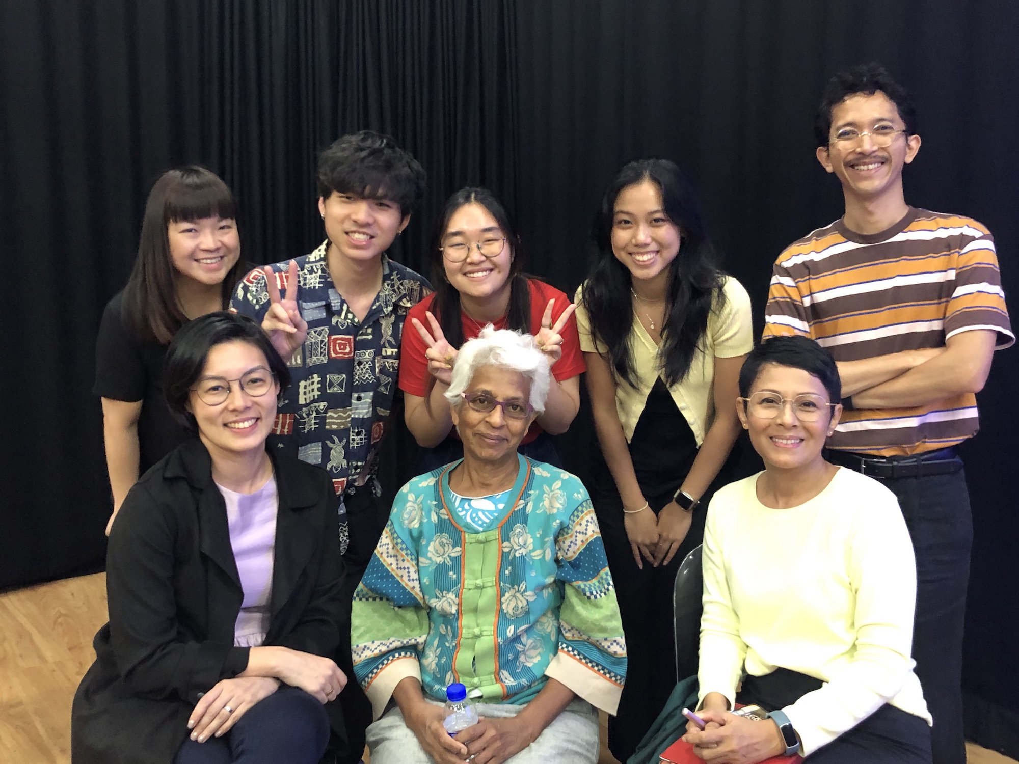 Eight persons, three seated and five standing behind them, smiling for a group photo.