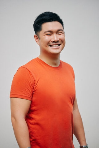 A male-presenting person in an orange shirt, smiling at the camera.