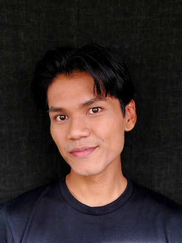 Headshot of Rino Junior John in a black shirt, smiling slightly into the camera.