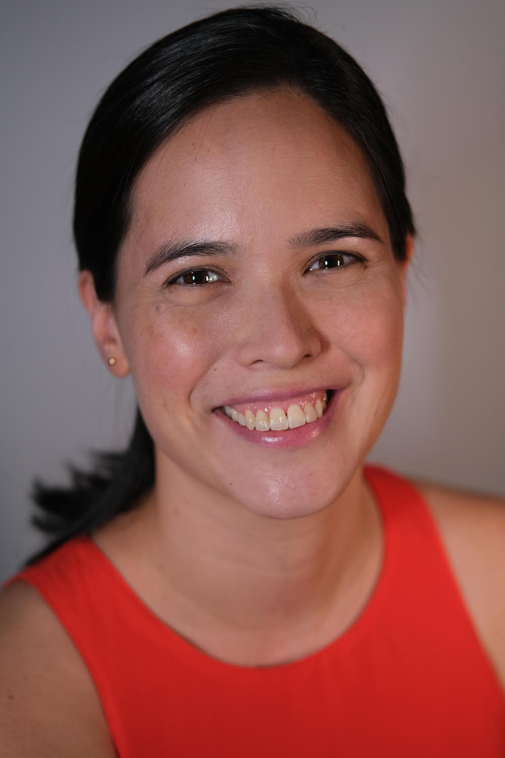 Headshot of Julie Wee in a sleeveless orange top, smiling wide at the camera.