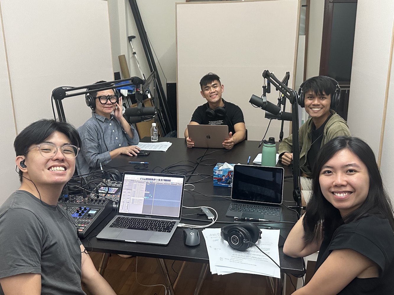 Five persons seated around a table with microphones positioned in front of two of them. They are smiling at the camera.