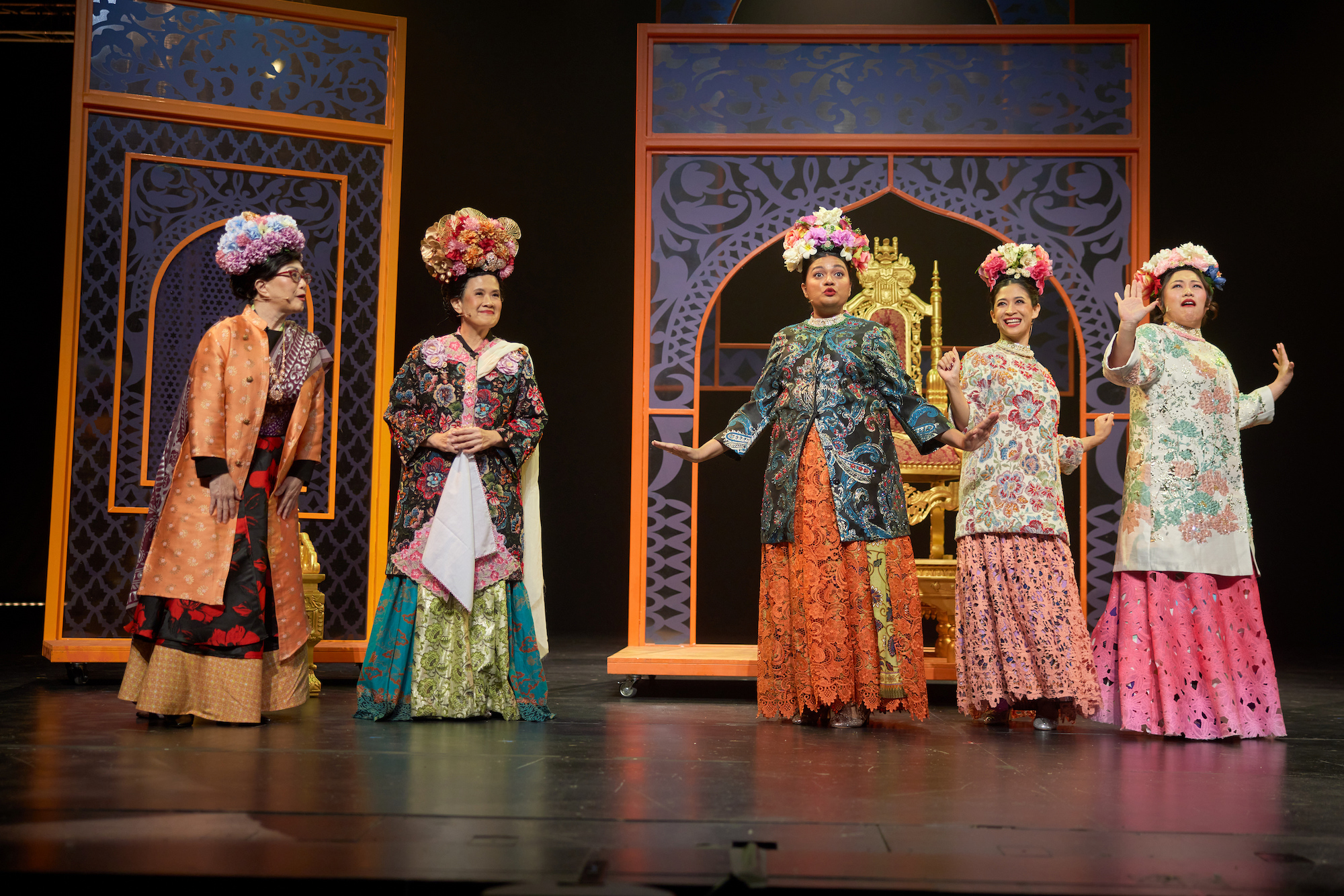 Five actors in elaborate, colourful Peranakan costumes lined up on stage in front of a large set.