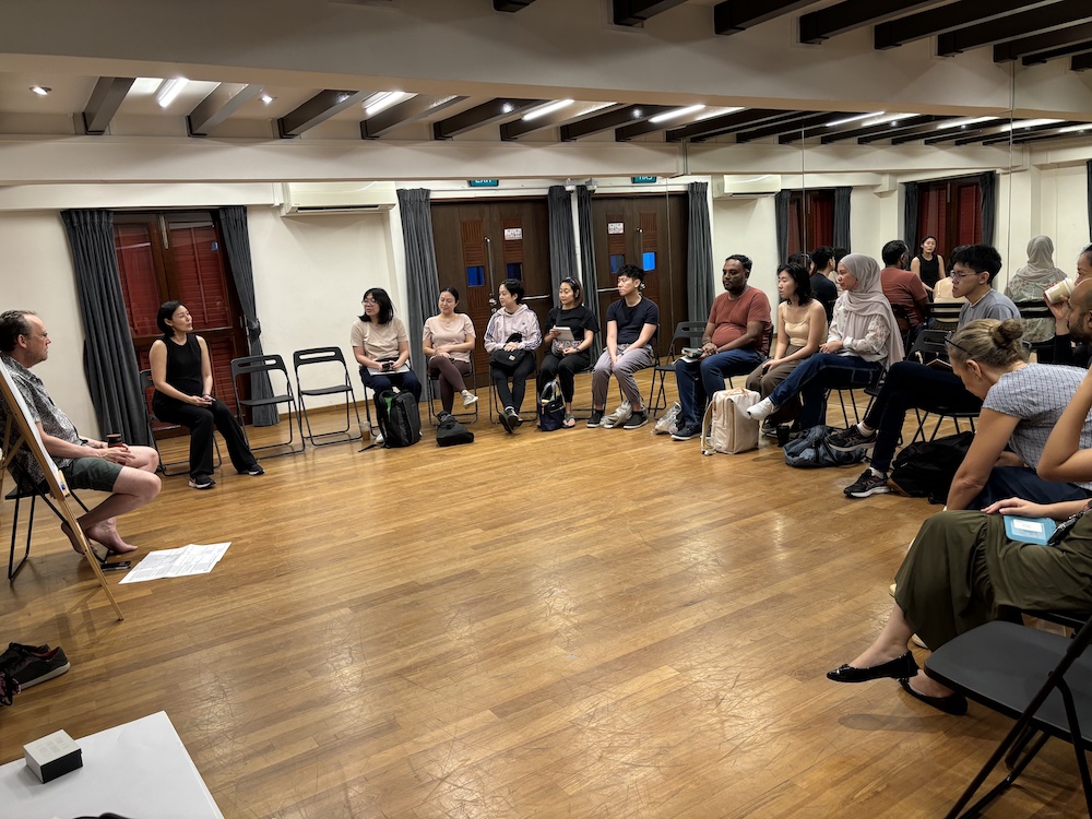 A semicircle of people seated in chairs, facing a person seated beside an easel. A semicircle of people seated in chairs, facing a person seated beside an easel.