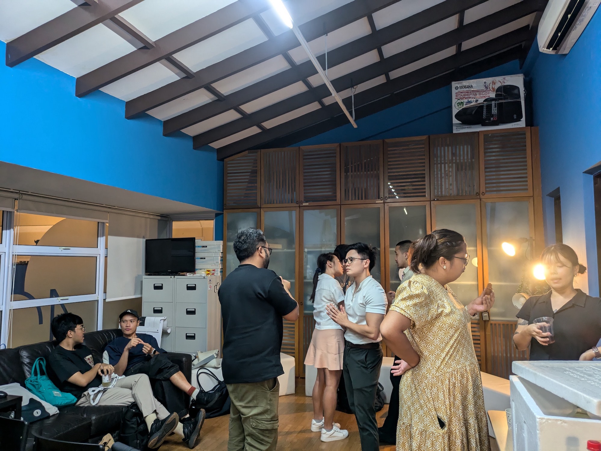 A small group of people standing around an office, speaking together in pairs and trios.