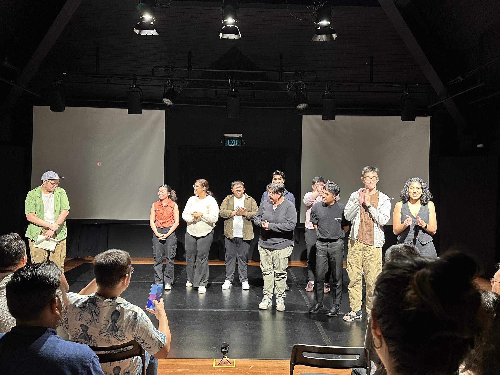 Eight people standing in a row in front of a small audience, clapping.