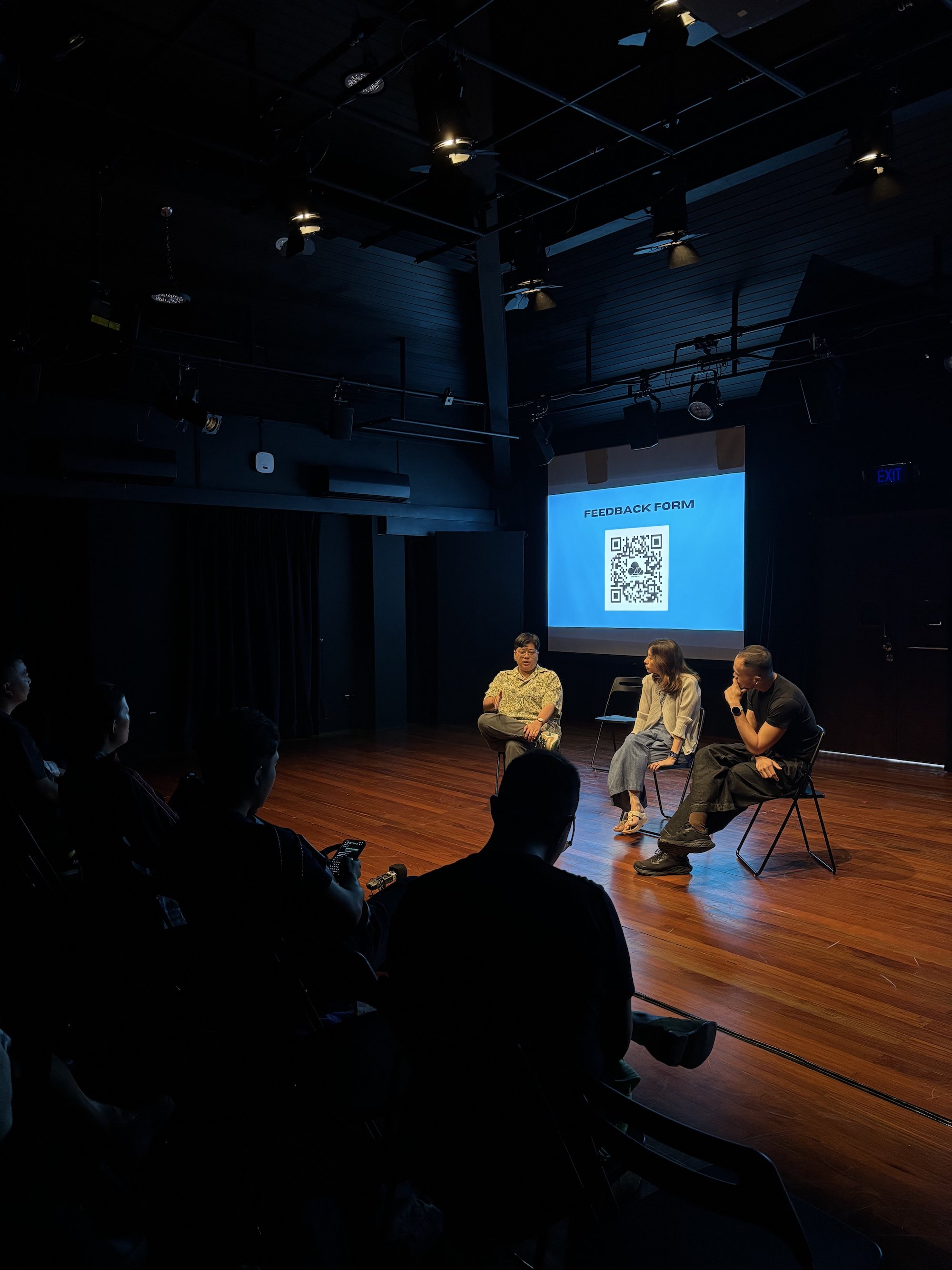 Three persons seated closely together in front of an audience, talking.