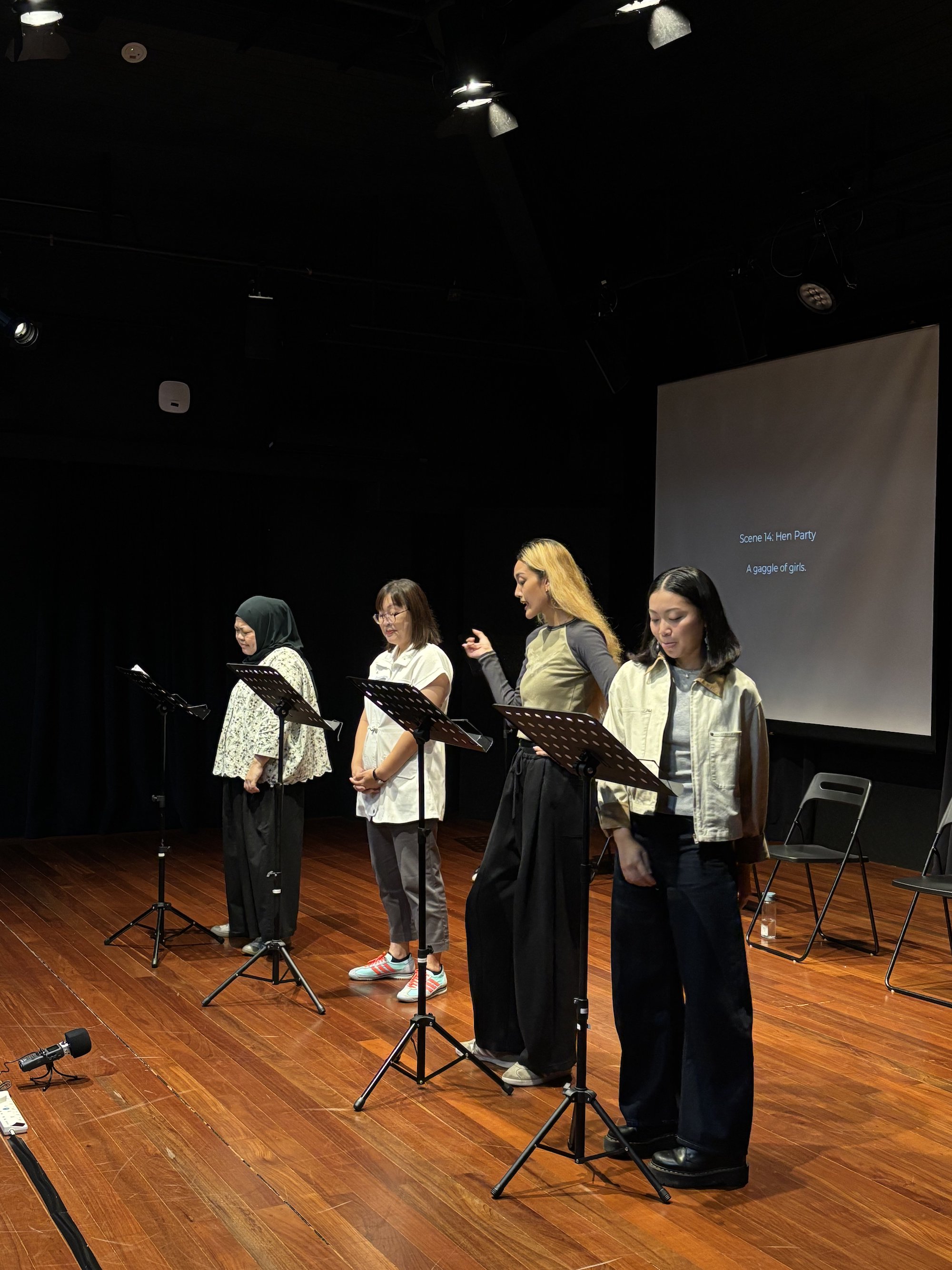 Four female-presenting persons standing in a row in front of music stands.