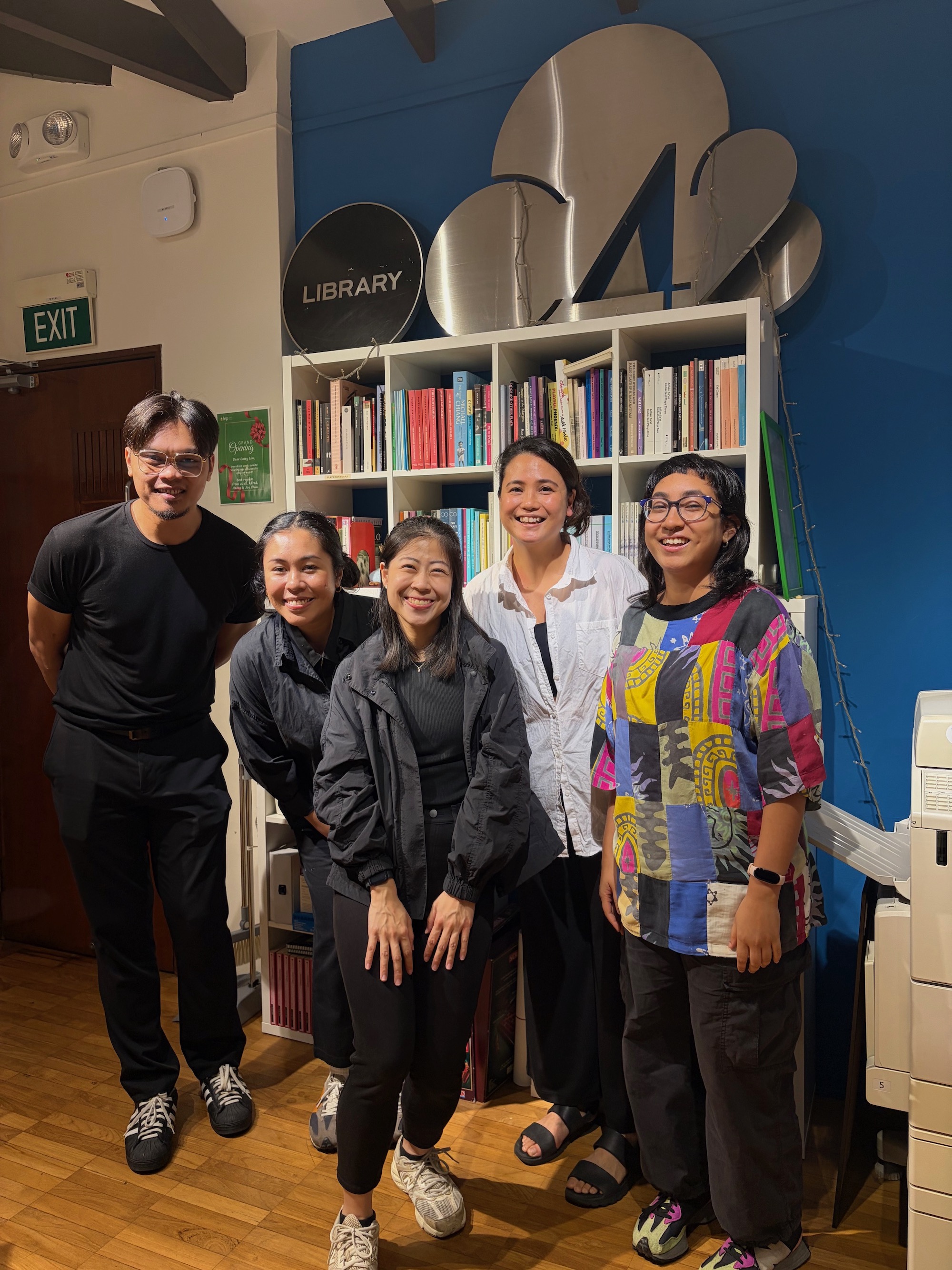 Five people standing in a row in front of a bookshelf, smiling.