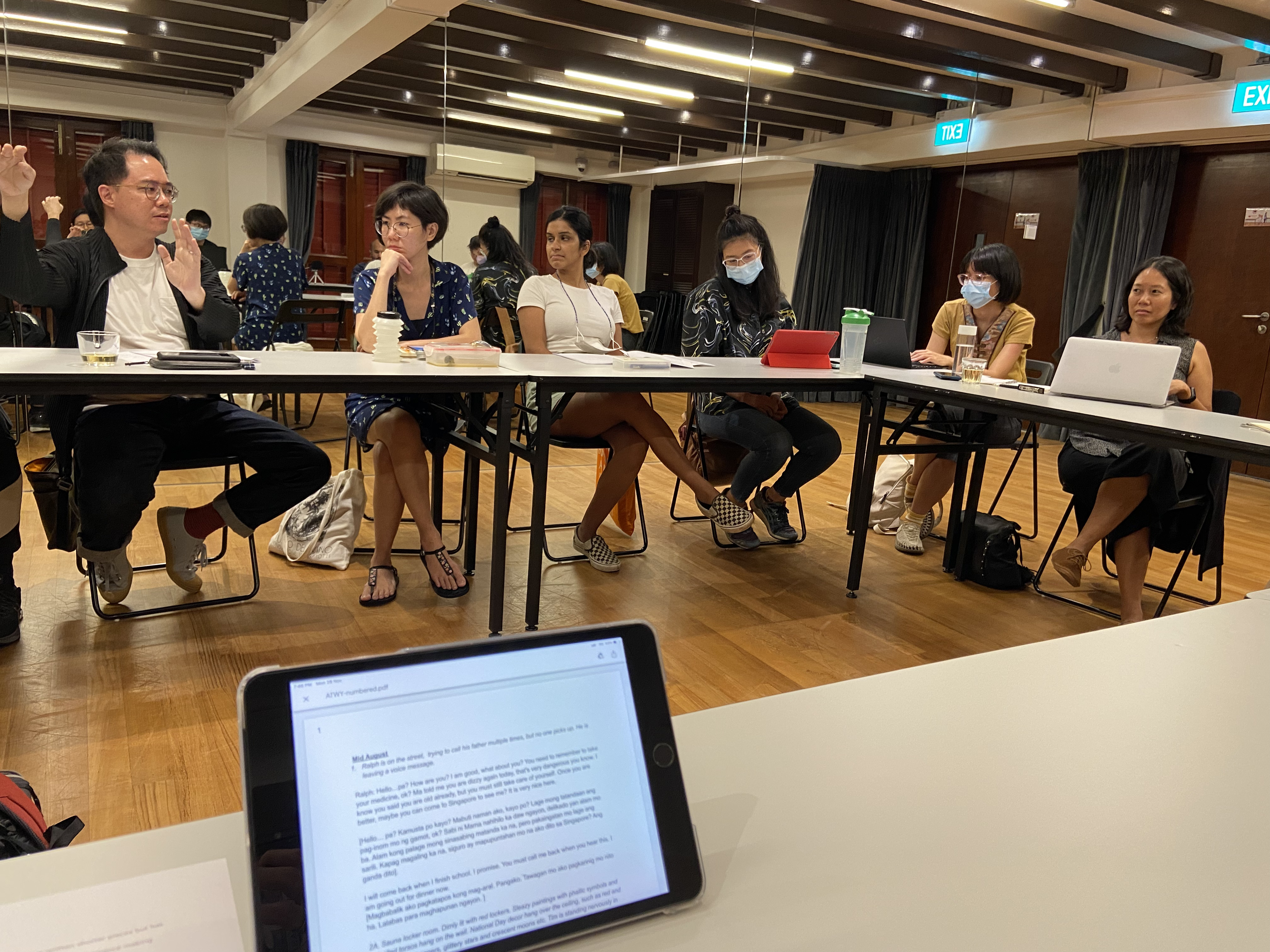 A photograph of six people seated in front of a long grey table, looking to be in thought and discussion.