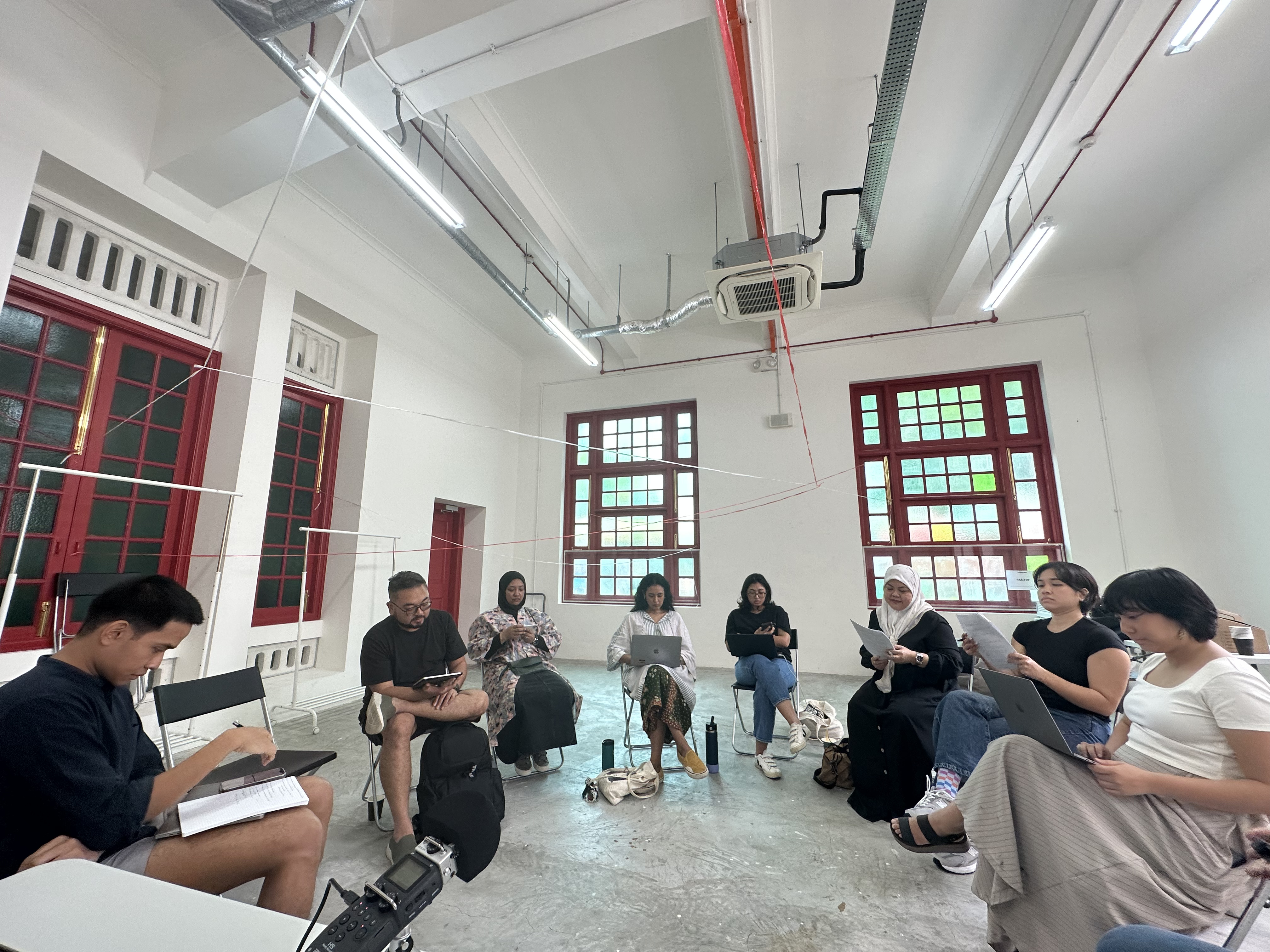 8 people seated in a circle reading from scripts or their devices. 