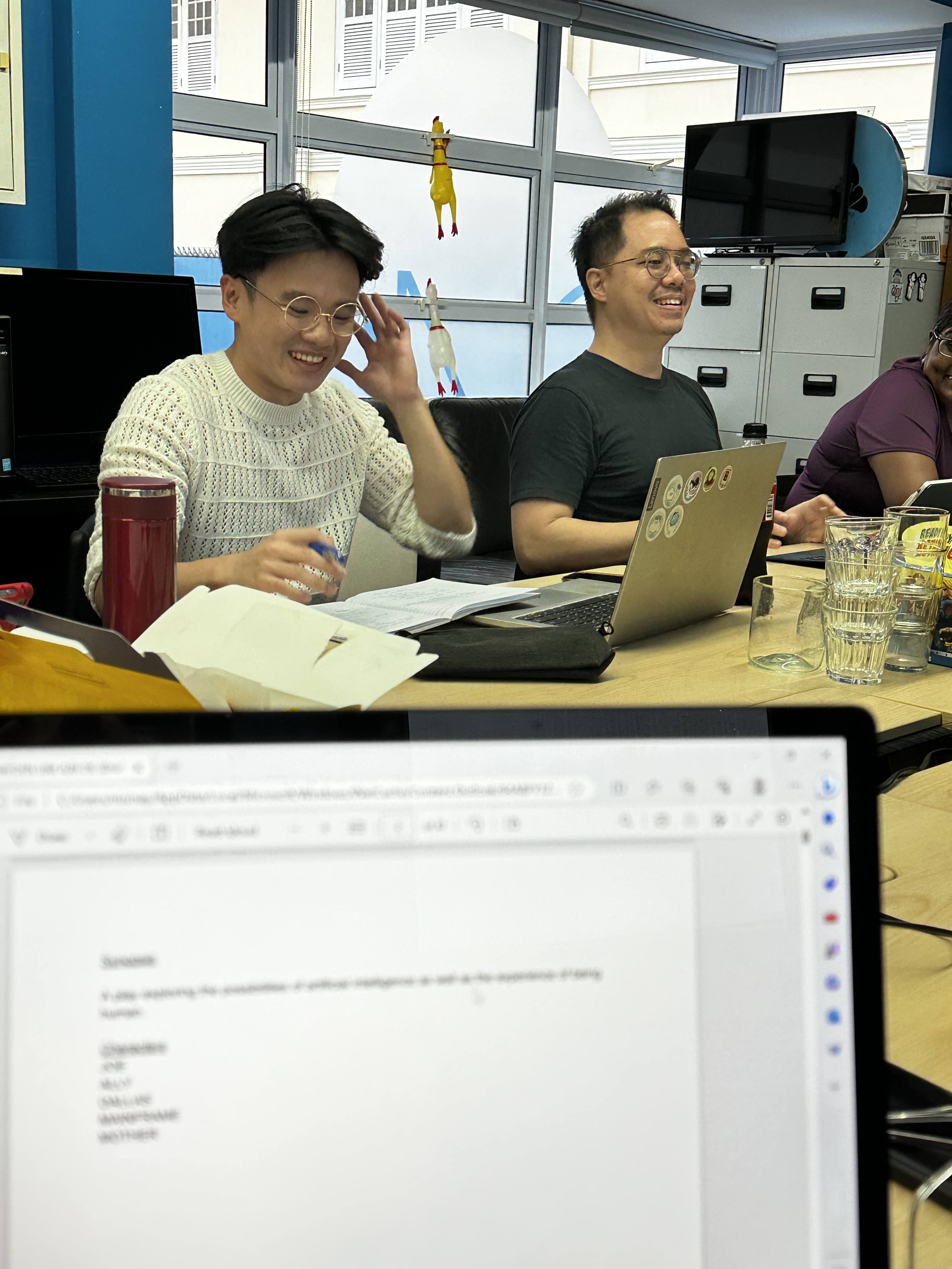 A photograph of Jun De, with a laptop in front of him, and Lucas, smiling.