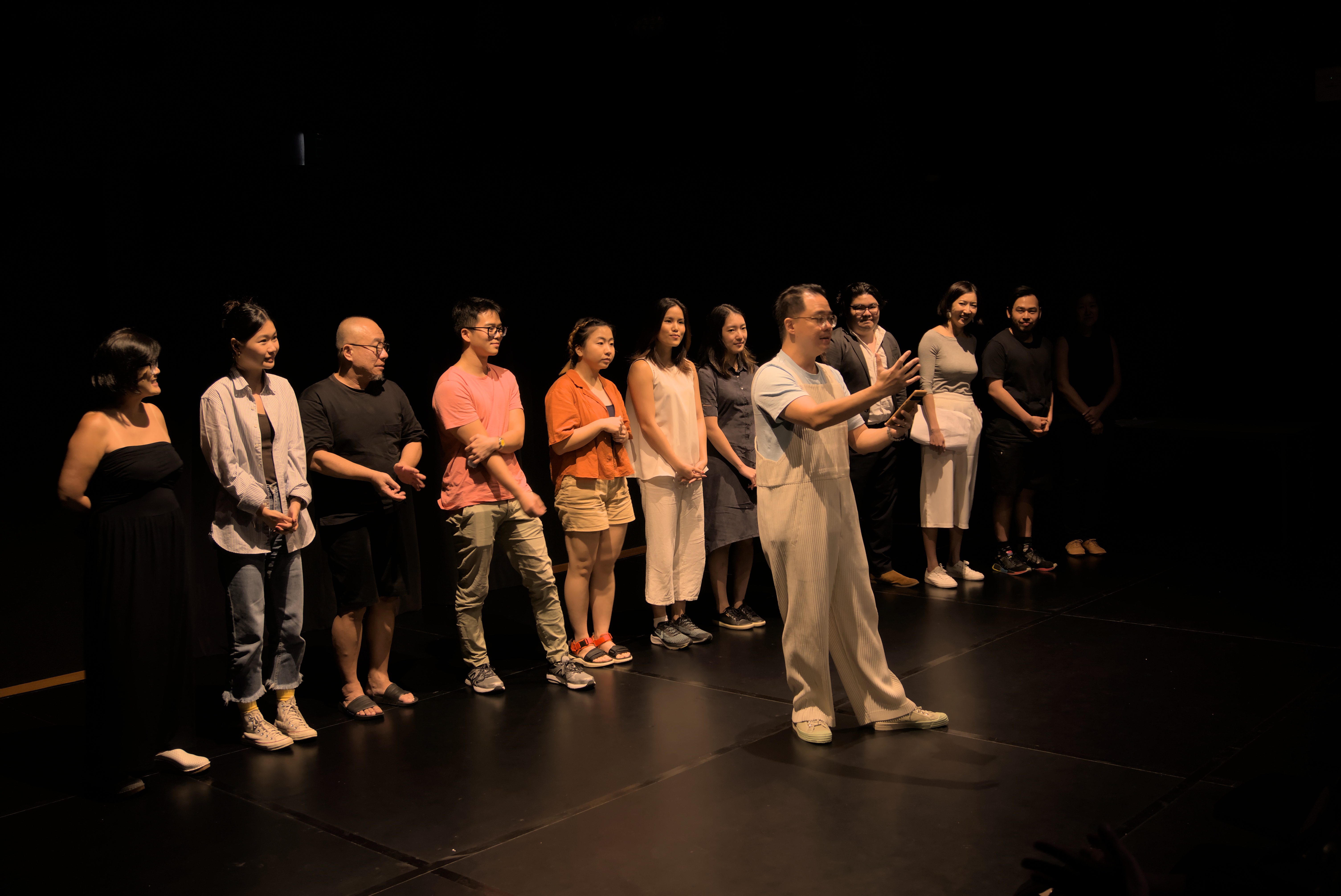 Playwrights, actors and directors for Headline Acts stand in a row with Lucas Ho standing in front of them for curtain call.